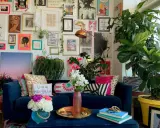 Ein Wohnzimmer im maximalistischen Stil mit einer blauen Couch, vielen Kissen, Pflanzen und einer Wand voller Kunstwerke und Drucke.