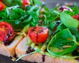Leckere Bruschetta mit Avocado, Tomaten und Rucola, beträufelt mit Balsamico. So lassen sich Balsamico-Flecken entfernen: schnell handeln!