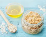 Zutaten für ein **Gesichtspeeling selber machen**: Haferflocken auf einem Holzlöffel, ein Glas mit Peeling und eine Schale mit Öl.