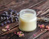 Ein Glas selbstgemachte Handcreme mit Lavendel und Rosenblüten auf Holzuntergrund.