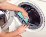 Hände reinigen die Gummidichtung der Waschmaschine mit einem blauen Tuch. Hausmittel helfen, die Waschmaschine zu reinigen und Gerüche zu vermeiden.