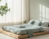 Ein ruhiges Schlafzimmer mit einem niedrigen Holzbett, bedeckt mit hellgrüner Bettwäsche. Die Wandfarbe und die Textilien harmonieren perfekt für ein Feng Shui Schlafzimmer.