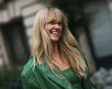 Lachende Frau mit **leichter Pony, lange Haare** und einem grünen Blazer.