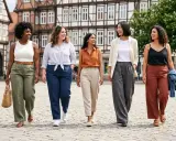 Fünf Frauen spazieren lächelnd über einen Platz. Sie zeigen, wie man Leinenhose kombinieren kann, in verschiedenen Farben und Styles.