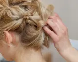 Eine Hand stylt blonde Haare zu verspielten hochsteckfrisuren mittellang. Kleine Zöpfe und gedrehte Strähnen ergeben einen lässigen Look.