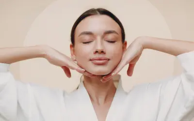 Frau mit geschlossenen Augen und einem sanften Lächeln, die ihr aufgedunsenes Gesicht mit den Händen massiert.