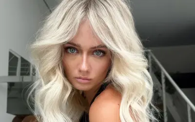 Blonde Frau mit voluminöser blowout frisur und blauen Augen blickt ernst in die Kamera.