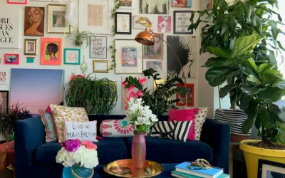 Ein Wohnzimmer im maximalistischen Stil mit einer blauen Couch, vielen Kissen, Pflanzen und einer Wand voller Kunstwerke und Drucke.