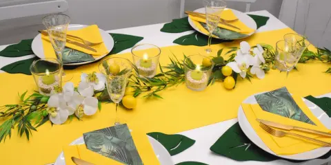 Sommerliche tischdeko mit zitronen, Orchideen und grünen Blättern. Kerzen in Gläsern sorgen für stimmungsvolles Licht.