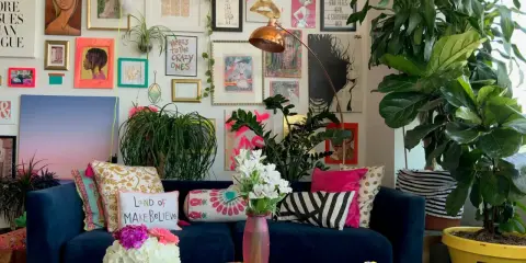 Ein Wohnzimmer im maximalistischen Stil mit einer blauen Couch, vielen Kissen, Pflanzen und einer Wand voller Kunstwerke und Drucke.