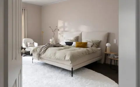 Beige schlafzimmer ideen: einladendes Bett mit beiger Bettwäsche, Akzentkissen und Decke. Weißer Sessel, Nachttische und Teppich schaffen Gemütlichkeit.