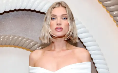 Blonde Frau mit einem lässigen, ripped bob Haarschnitt und blauen Augen, trägt ein weißes Kleid.