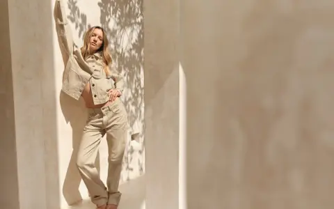 Frau in beiger Hose und Jacke, die lässig posiert. Ein Beispiel, wie man beige Hose kombinieren kann für einen stilvollen Look.