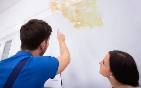 Mann prüft Stockflecken an der Wand, um sie zu entfernen. Eine Frau schaut besorgt zu.