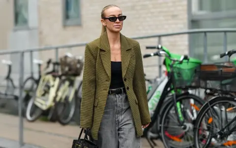 Stilvolle Frau mit Sonnenbrille und kariertem Blazer, die zeigt, wie man graue Jeans kombiniert.