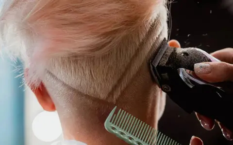 Eine Frau bekommt einen modernen Undercut. Haare werden mit einem Trimmer geschnitten, ein Kamm hält die Strähnen.