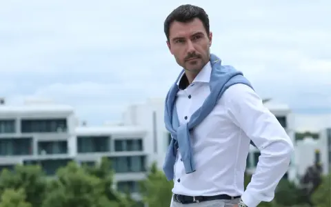 Mann mit klassischer old money hairstyle herren, trägt weißes Hemd und blauen Pullover über den Schultern.