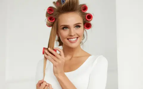 Lächelnde Frau mit roten Wicklern im Haar, die sich Locken macht.