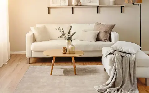Ein helles Wohnzimmer mit weißem Sofa, Holztisch und Teppich. Perfekt für minimalistisch wohnen.