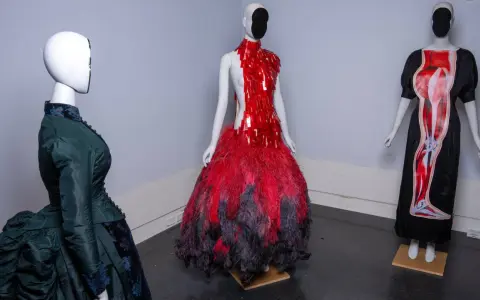 Drei Schaufensterpuppen präsentieren extravagante Kleider, die an das Met Gala Thema erinnern: eines in Grün im viktorianischen Stil, eines in Rot mit Federn und eines mit anatomischem Druck.