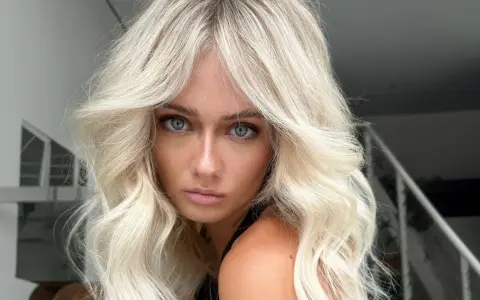 Blonde Frau mit voluminöser blowout frisur und blauen Augen blickt ernst in die Kamera.