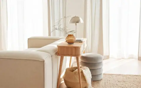Gemütliches Wohnzimmer mit beigem Sofa, Holztisch, Lampe und Korb. Die helle Atmosphäre vermittelt das Gefühl von Hygge Bedeutung: Wohlbefinden und Gemütlichkeit.