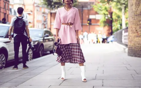 Ein Midirock kombiniert mit einem rosa Pullover und weißen Stiefeln – ein lässiger Sommer-Look auf der Straße.