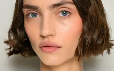 Nahaufnahme einer Frau mit einem kurzen Bob-Haarschnitt, blauen Augen und rosafarbenen Wangen.