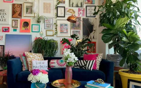 Ein Wohnzimmer im maximalistischen Stil mit einer blauen Couch, vielen Kissen, Pflanzen und einer Wand voller Kunstwerke und Drucke.