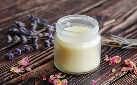 Ein Glas selbstgemachte Handcreme mit Lavendel und Rosenblüten auf Holzuntergrund.