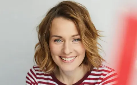 Eine Frau mit schulterlangen, welligen Haaren und einem strahlenden Lächeln. Diese Frisuren 2026 halblang sind modern und schmeichelhaft.
