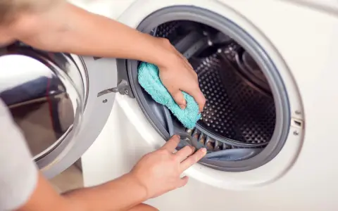 Hände reinigen die Gummidichtung der Waschmaschine mit einem blauen Tuch. Hausmittel helfen, die Waschmaschine zu reinigen und Gerüche zu vermeiden.