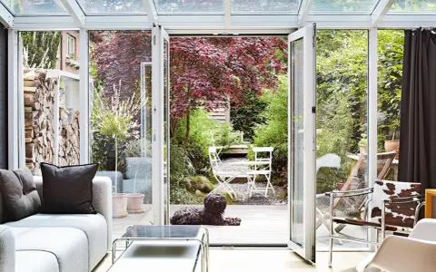 Gemütliche Wintergarten einrichten Ideen: Hund liegt auf Holzterrasse vor Garten mit rotem Ahornbaum und weißem Mobiliar.