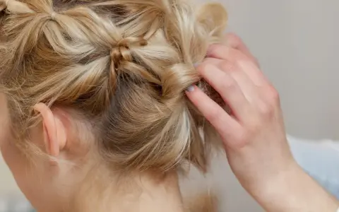 Eine Hand stylt blonde Haare zu verspielten hochsteckfrisuren mittellang. Kleine Zöpfe und gedrehte Strähnen ergeben einen lässigen Look.