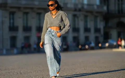 Stylische Frau in weit geschnittenen Jeans und kurzem Strickpullover, die zeigt, wie man wide leg jeans kombinieren kann.