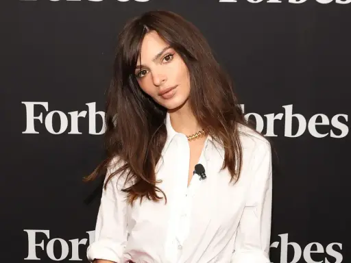 Emily Ratajkowski mit langen, gestuften Haaren und einem weißen Hemd vor einem Forbes-Banner.
