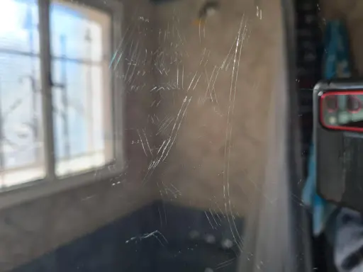 Zahlreiche Kratzer auf einer Glasoberfläche, die auf eine Politur warten. Im Hintergrund ist ein Fenster mit Jalousien zu sehen.