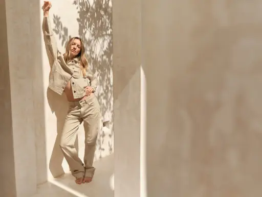 Frau in beiger Hose und Jacke, die lässig posiert. Ein Beispiel, wie man beige Hose kombinieren kann für einen stilvollen Look.