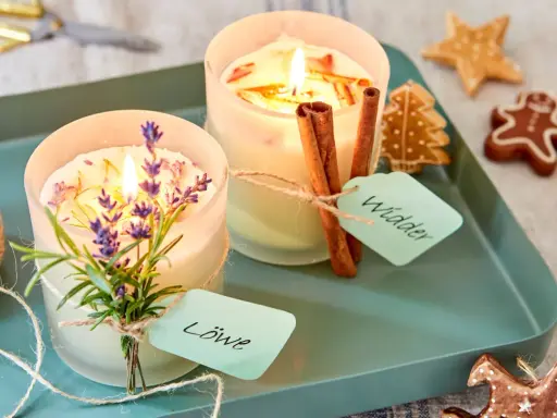 Zwei selbstgemachte Duftkerzen mit Lavendel und Zimtstangen, verziert mit Lebkuchen.