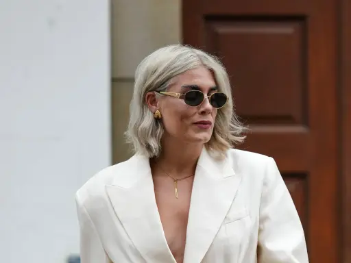Moderne Frau mit gestuften Frisuren ab 50 mit Brille, trägt cremefarbenen Blazer und auffälligen Schmuck.