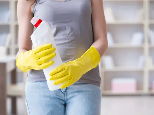 Person in gelben Handschuhen hält Reinigungsmittel. So putzt man Fenster streifenfrei für ein strahlendes Ergebnis.