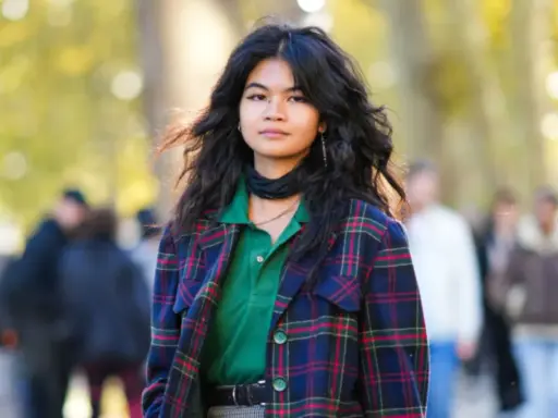 Junge Frau mit voluminösem, flauschigem Haar, trägt karierten Blazer und grünes Poloshirt.