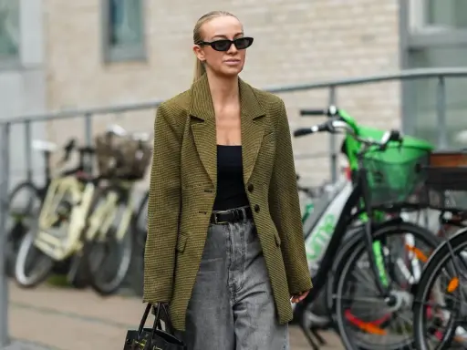 Stilvolle Frau mit Sonnenbrille und kariertem Blazer, die zeigt, wie man graue Jeans kombiniert.