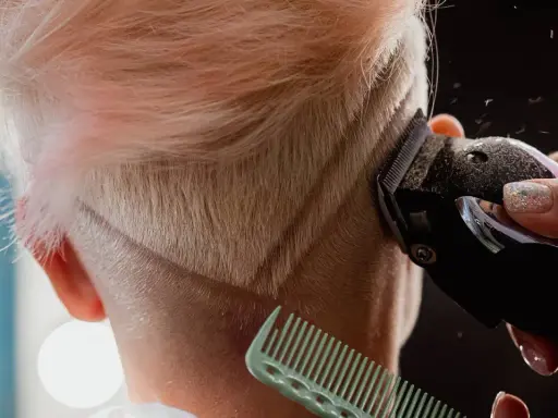 Eine Frau bekommt einen modernen Undercut. Haare werden mit einem Trimmer geschnitten, ein Kamm hält die Strähnen.