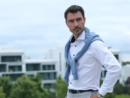 Mann mit klassischer old money hairstyle herren, trägt weißes Hemd und blauen Pullover über den Schultern.