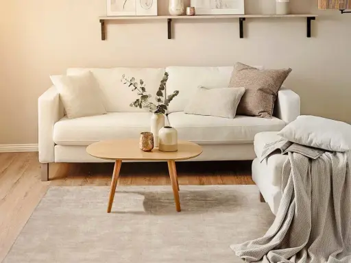 Ein helles Wohnzimmer mit weißem Sofa, Holztisch und Teppich. Perfekt für minimalistisch wohnen.