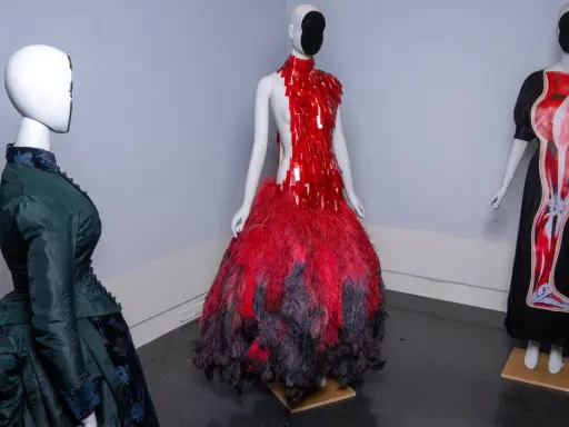 Drei Schaufensterpuppen präsentieren extravagante Kleider, die an das Met Gala Thema erinnern: eines in Grün im viktorianischen Stil, eines in Rot mit Federn und eines mit anatomischem Druck.
