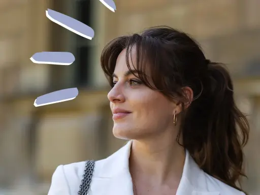 Frau mit rundem Gesicht und Curtain Bangs, trägt weißen Blazer.