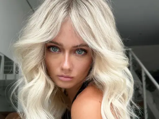 Blonde Frau mit voluminöser blowout frisur und blauen Augen blickt ernst in die Kamera.