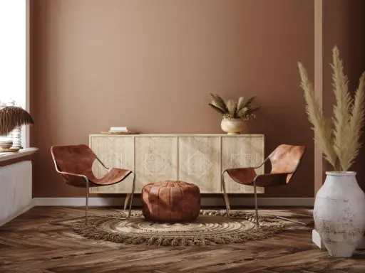 Ein gemütliches Wohnzimmer im Boho-Stil mit zwei Ledersesseln, einem runden Teppich, einem Sideboard und Trockenblumen.